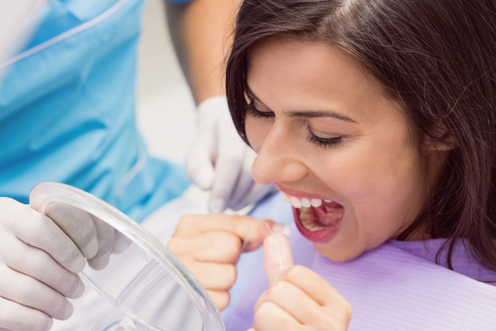 woman in dental clinic flossing with a mirror in front of her