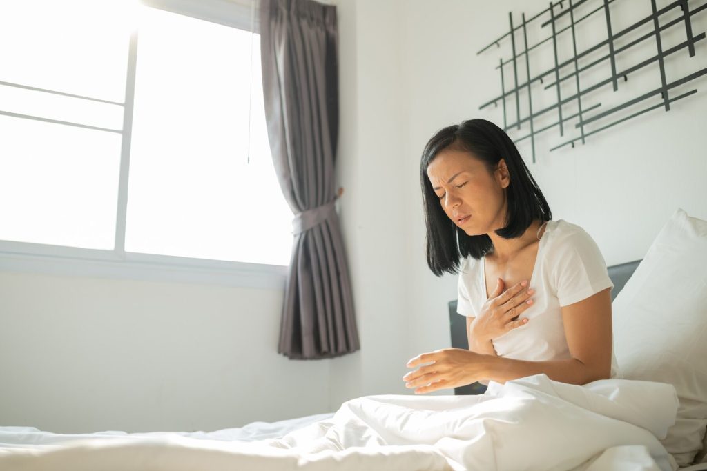 woman feeling unwell in bed with hand to her chest