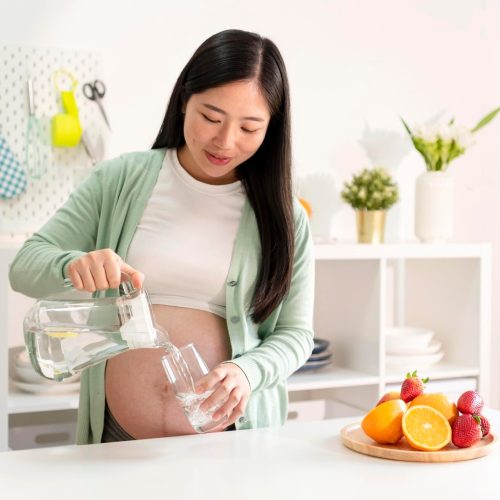 pregnant woman pouring water into a cup inside a kitchen