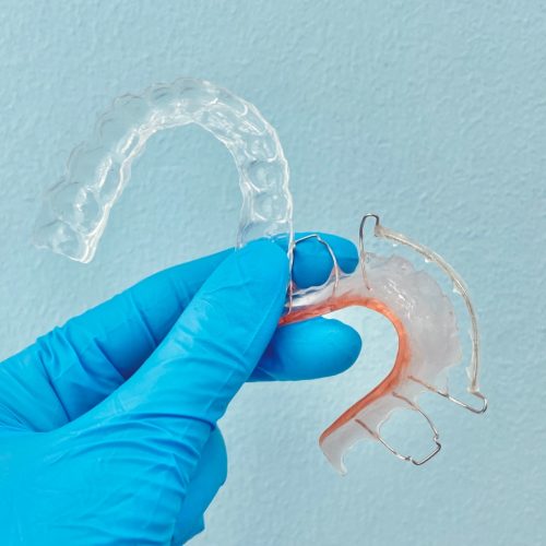 gloved hand holding hawley retainer and clear retainer